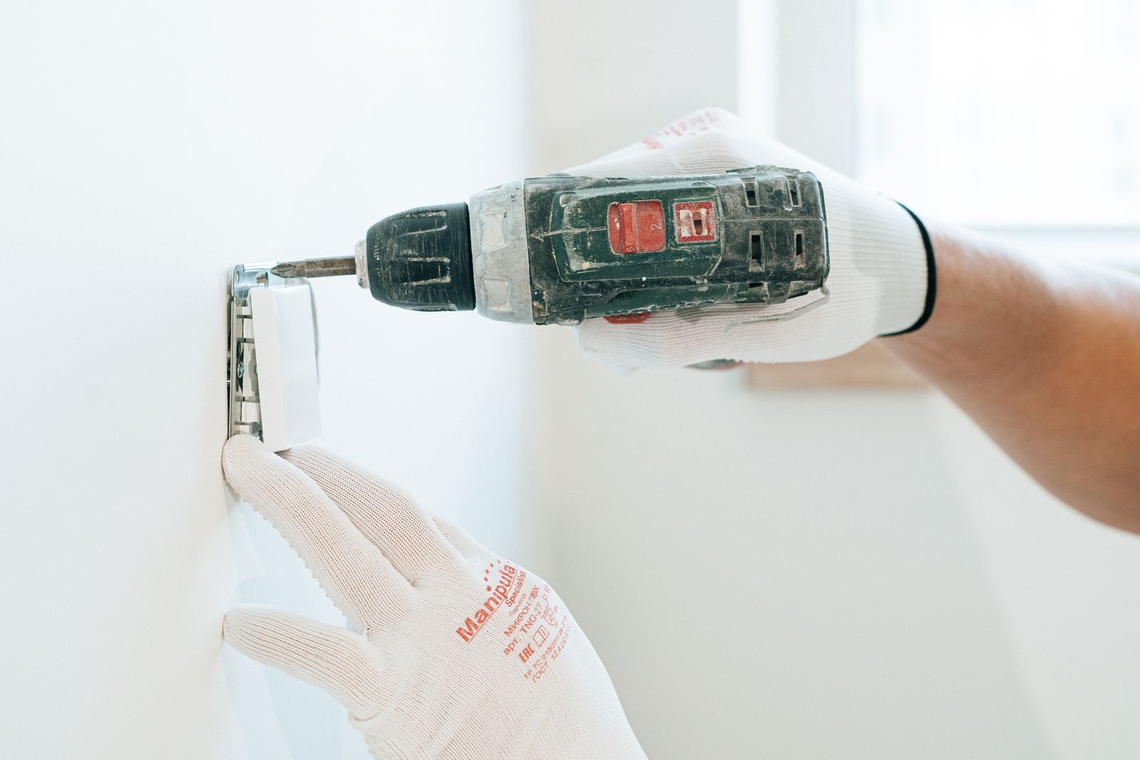 An electrician terminating the conductors behind a wall outlet during a replacement.